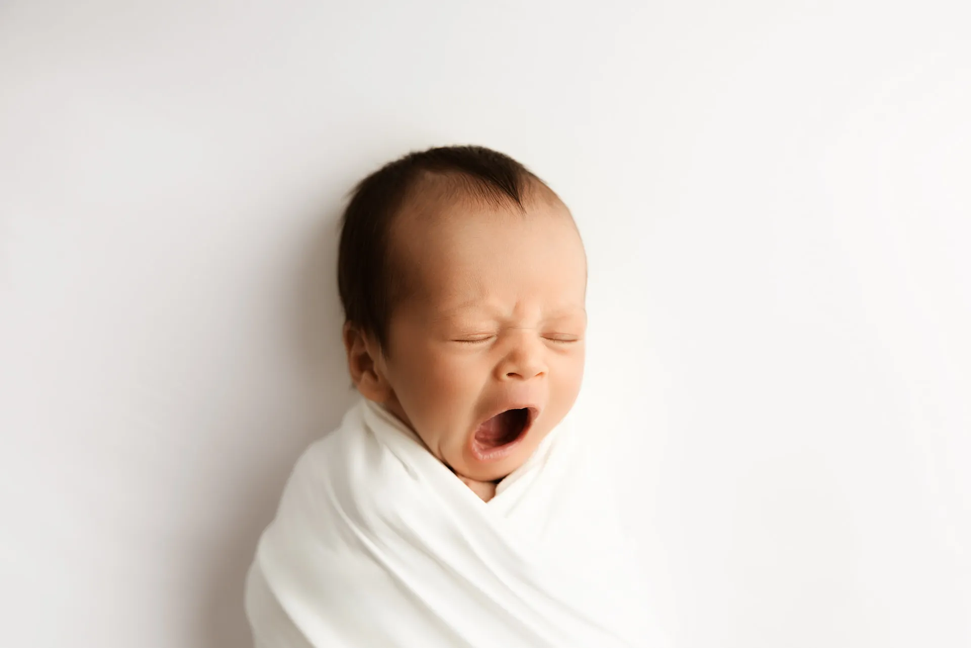 Newborn baby yawning while wrapped in white fabric - newborn photography Kingston upon Thames