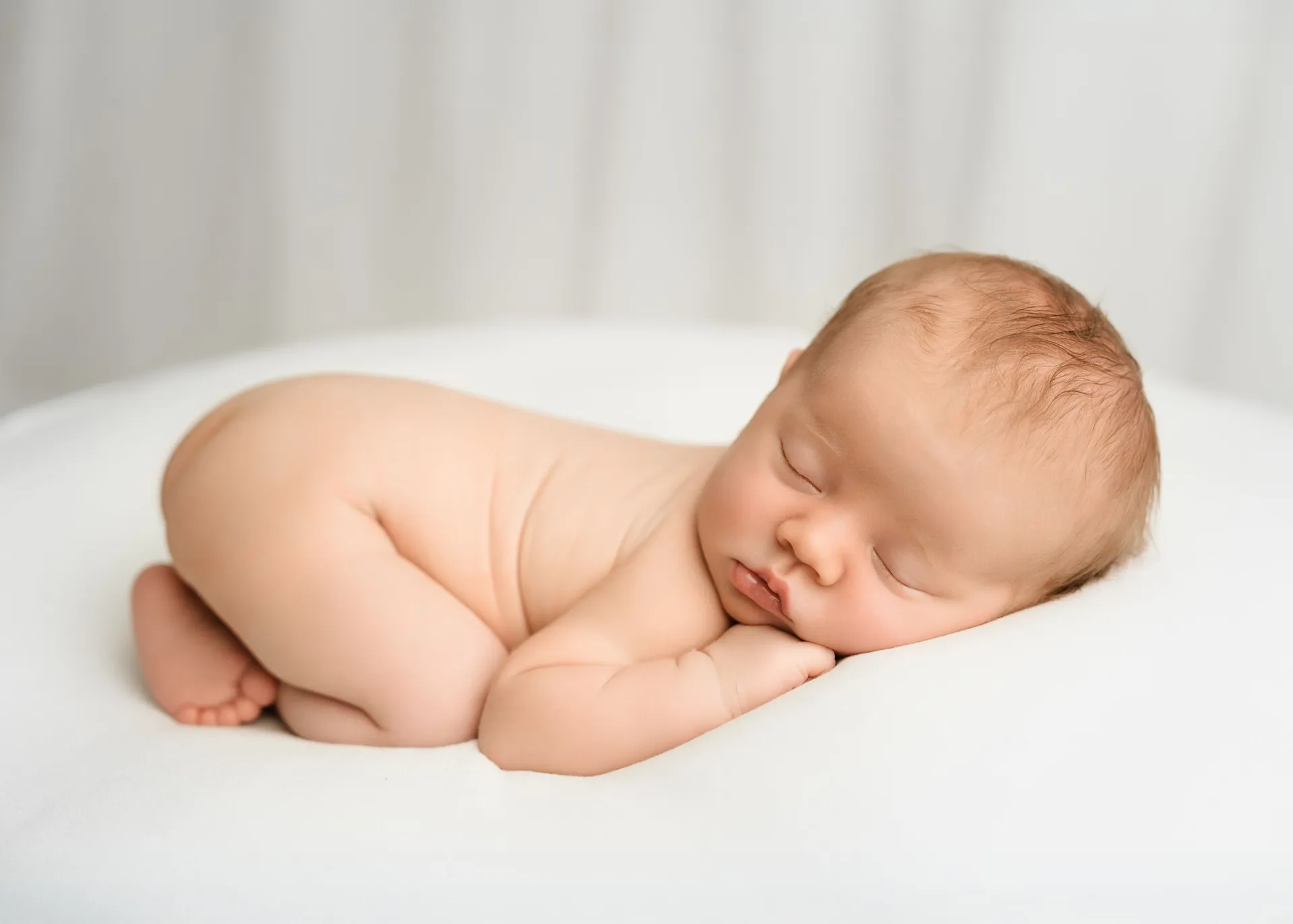 Sleeping newborn lying on side against soft white background - baby photographer Kingston