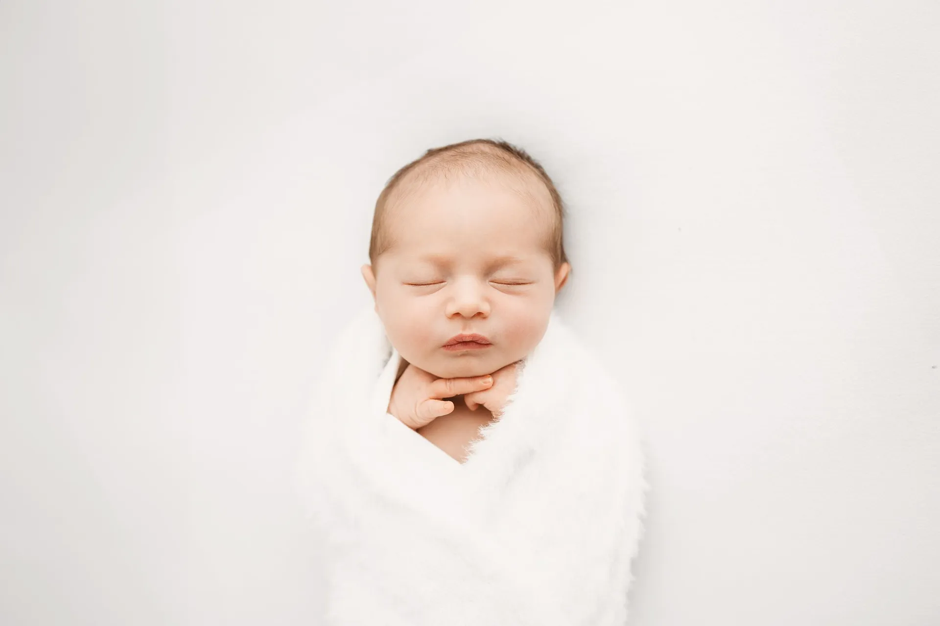 Peaceful sleeping newborn baby swaddled in white fabric - newborn photography Surrey
