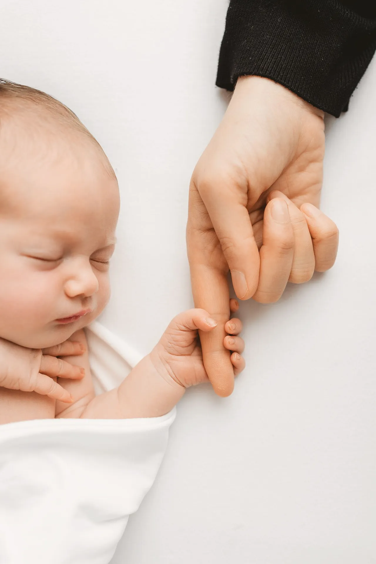 Close-up of tiny newborn hand grasping adult finger