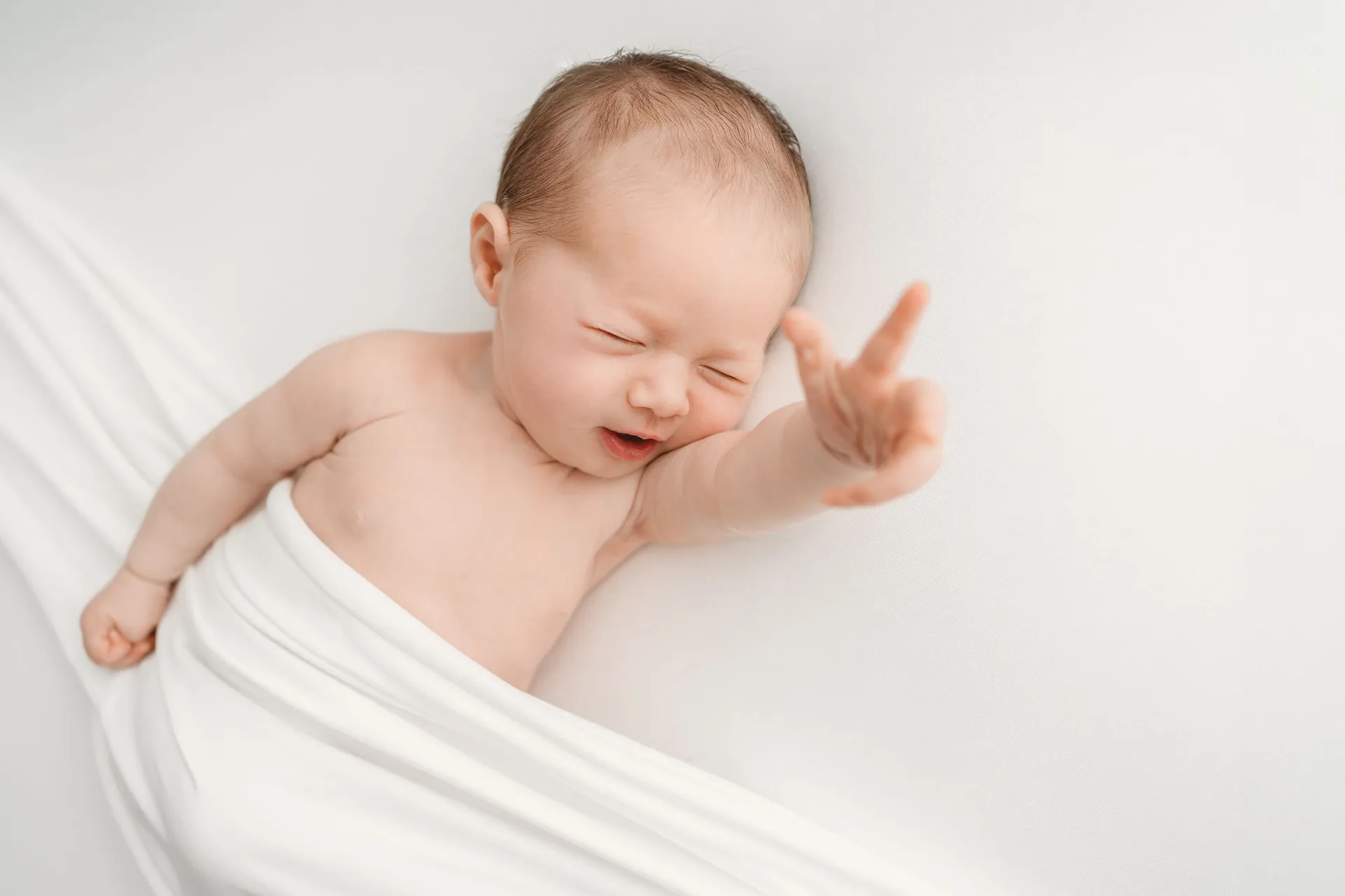 Smiling newborn baby wrapped in white fabric
