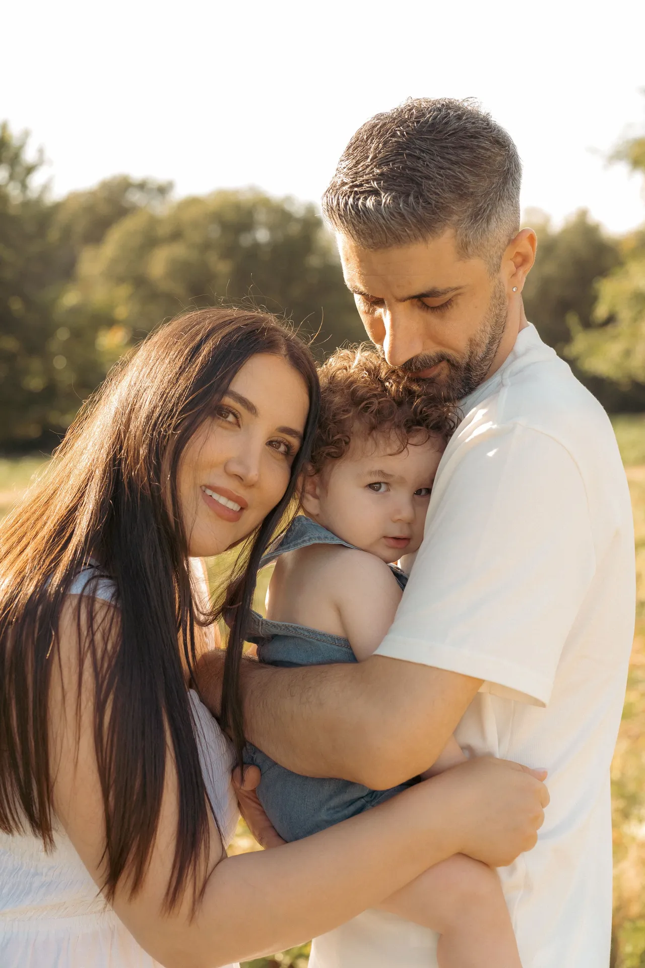 Parents embrace their young child in a sun-drenched outdoor setting