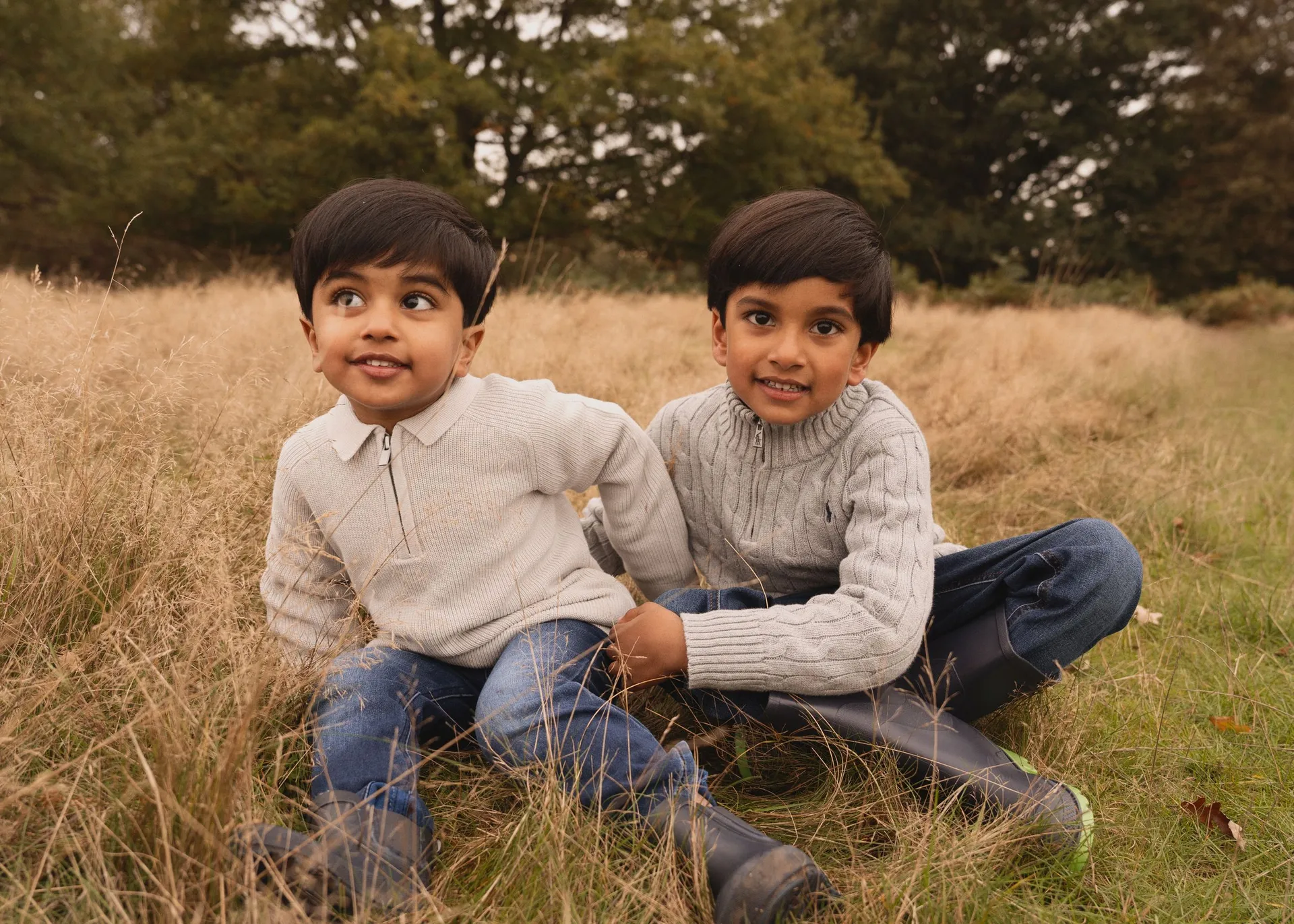 Two children in sweaters sitting together in golden autumn grass