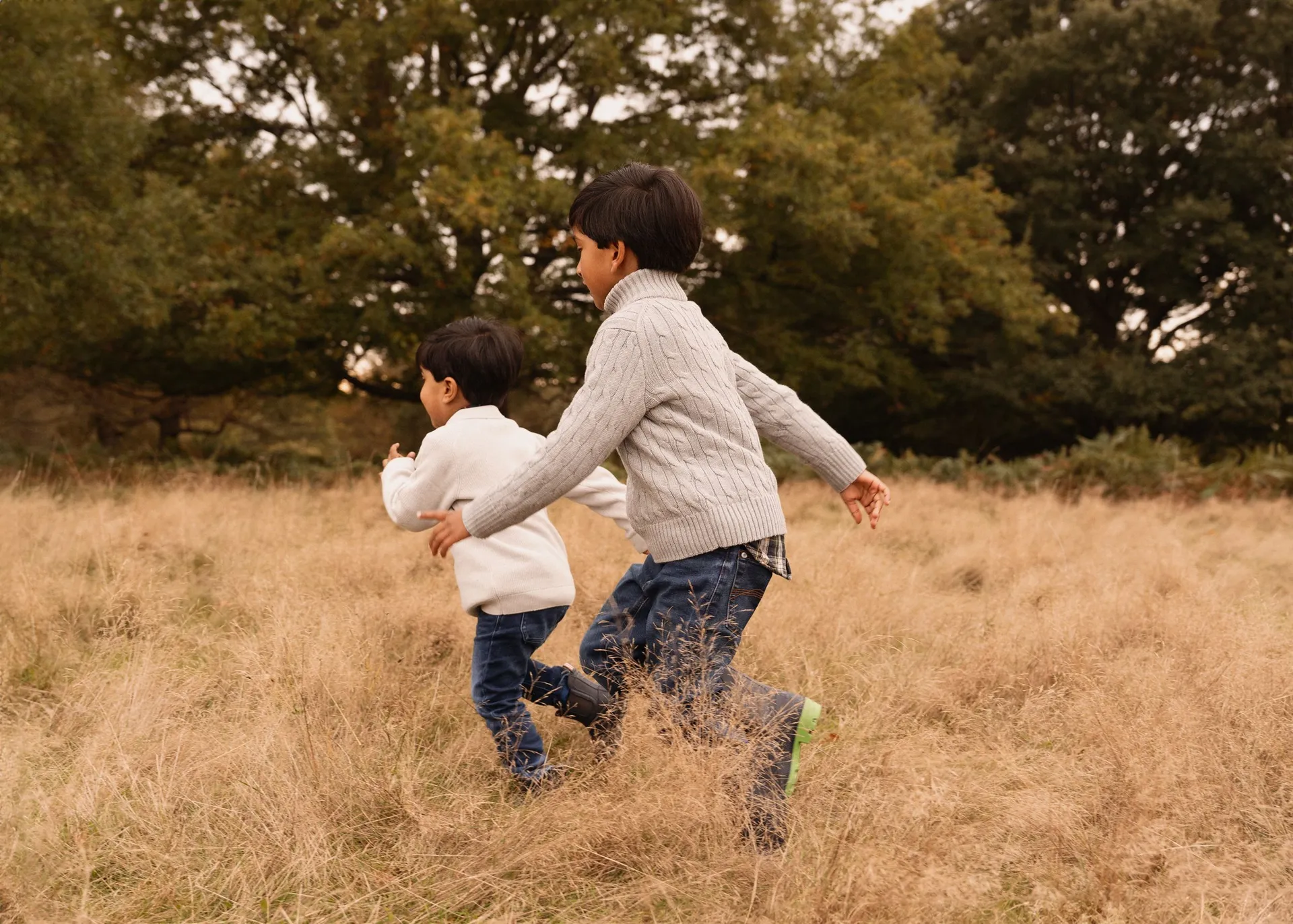 Two people running together through tall grass in autumn field at sunset