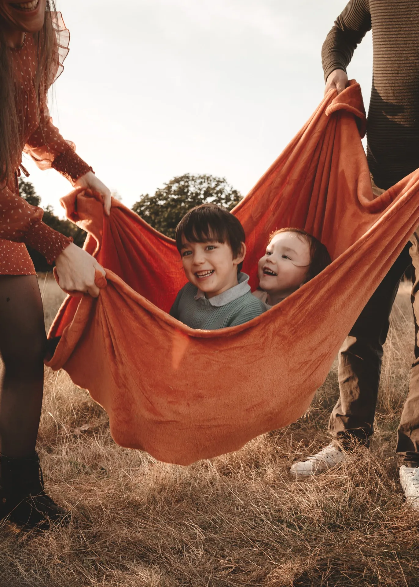 Two children laughing while being swung in a blanket outdoors