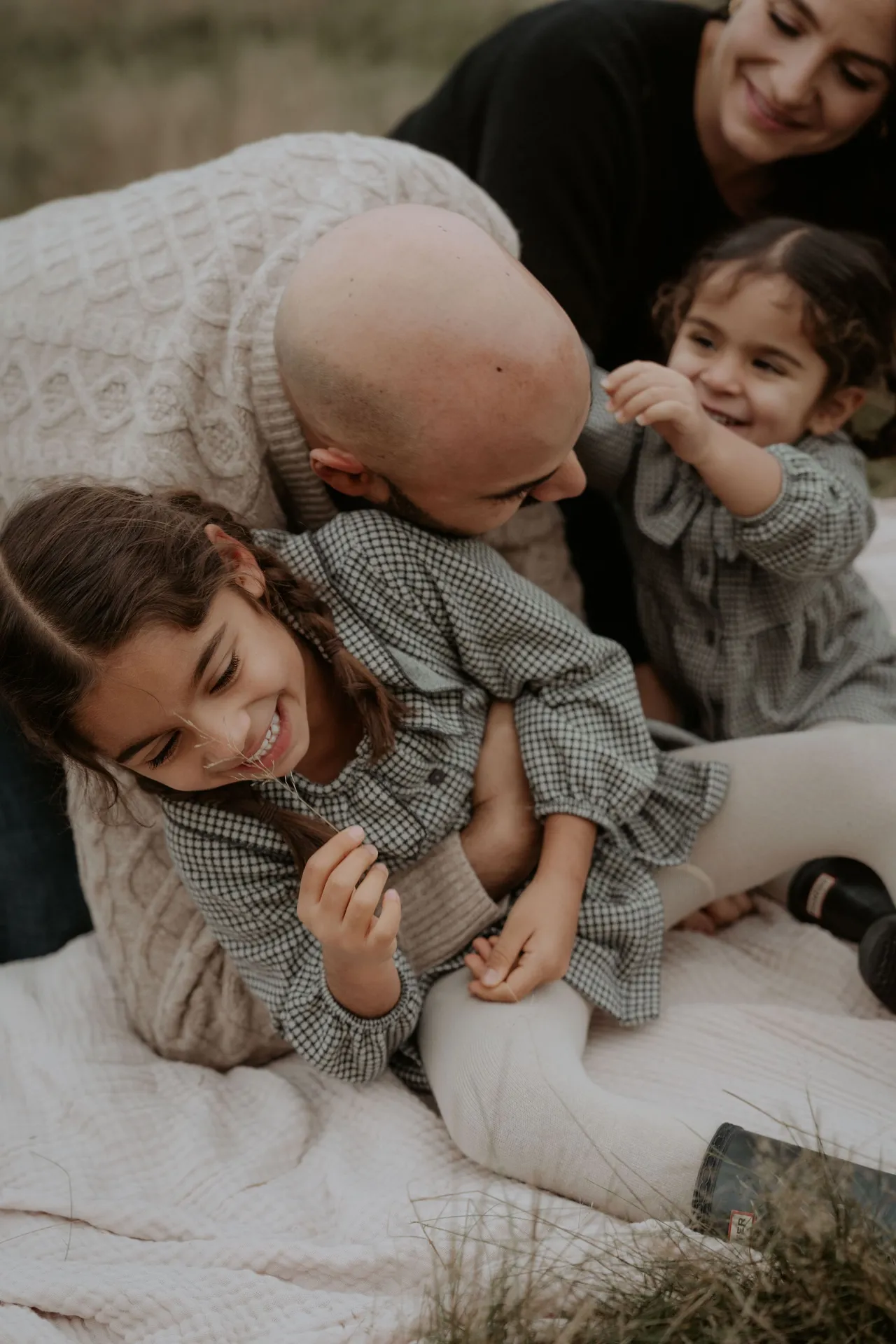 Family lying on blanket during playful tickle session outdoors