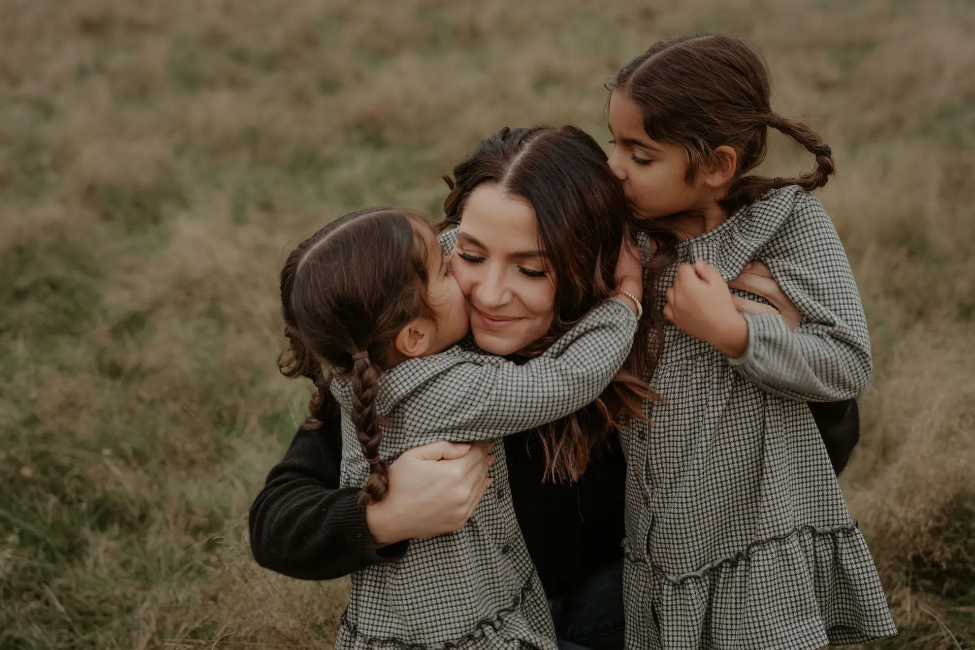 Family members share joyful hugs and kisses in a candid outdoor moment
