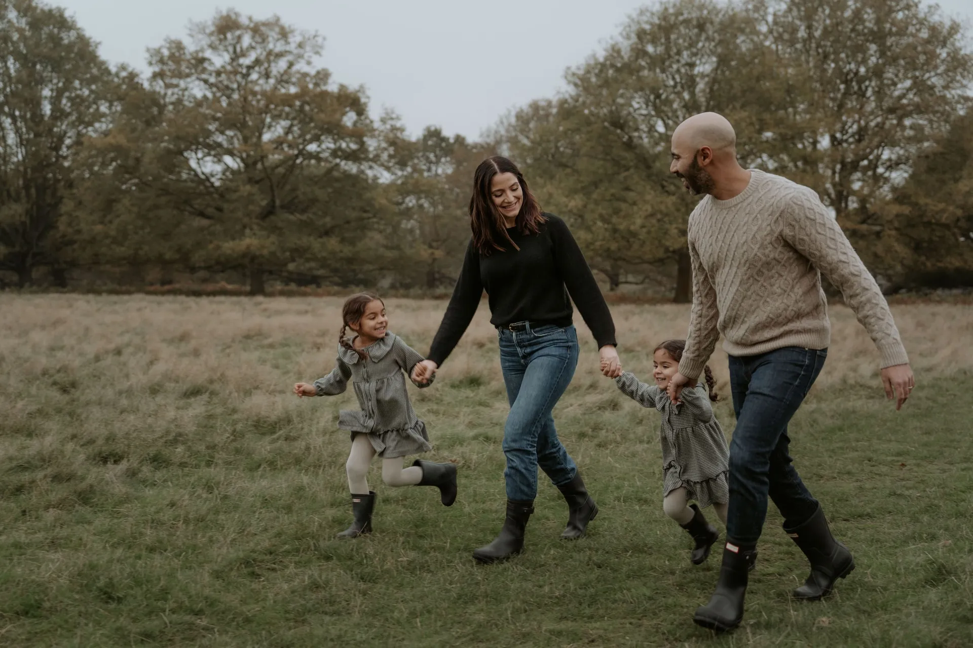 Family holding hands while running together through grassy field