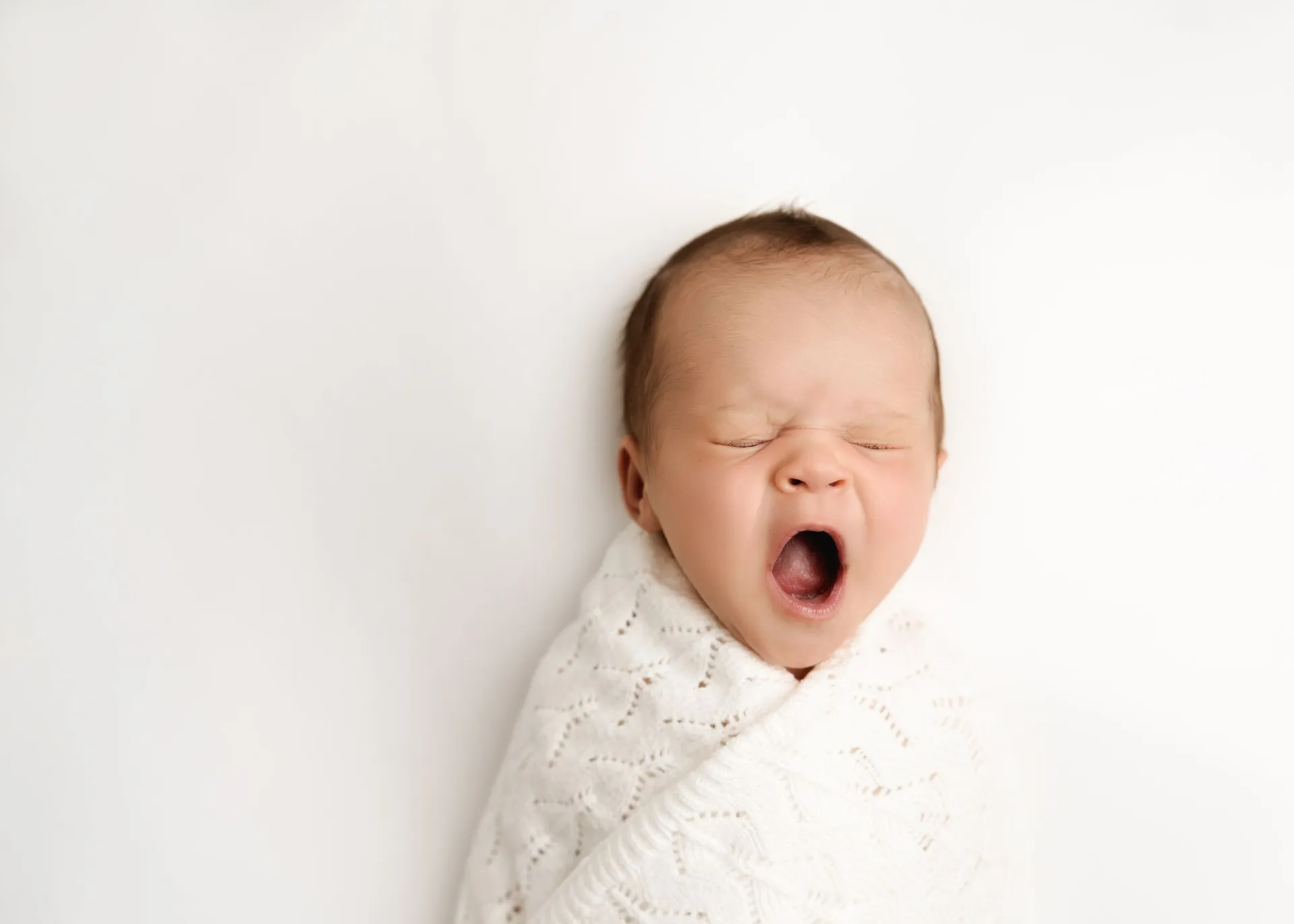 Yawning newborn wrapped in white knit blanket