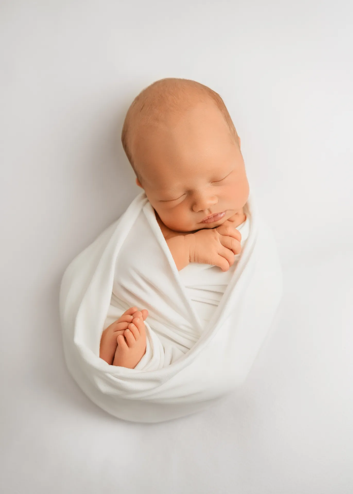 Newborn baby swaddled in white wrap sleeping peacefully - newborn photographer Kingston