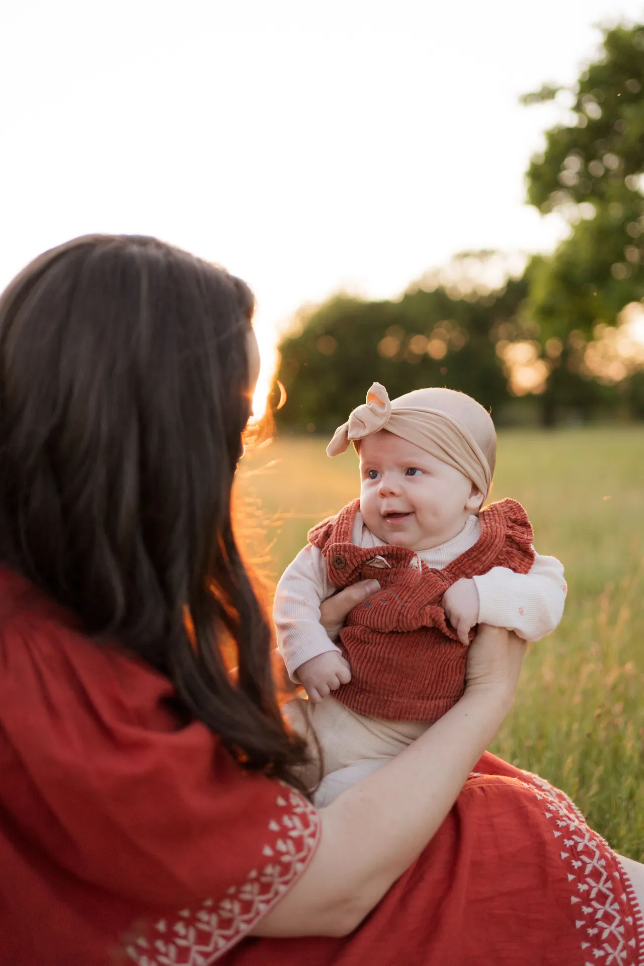 Baby wearing rust-colored outfit smiles during golden hour in field